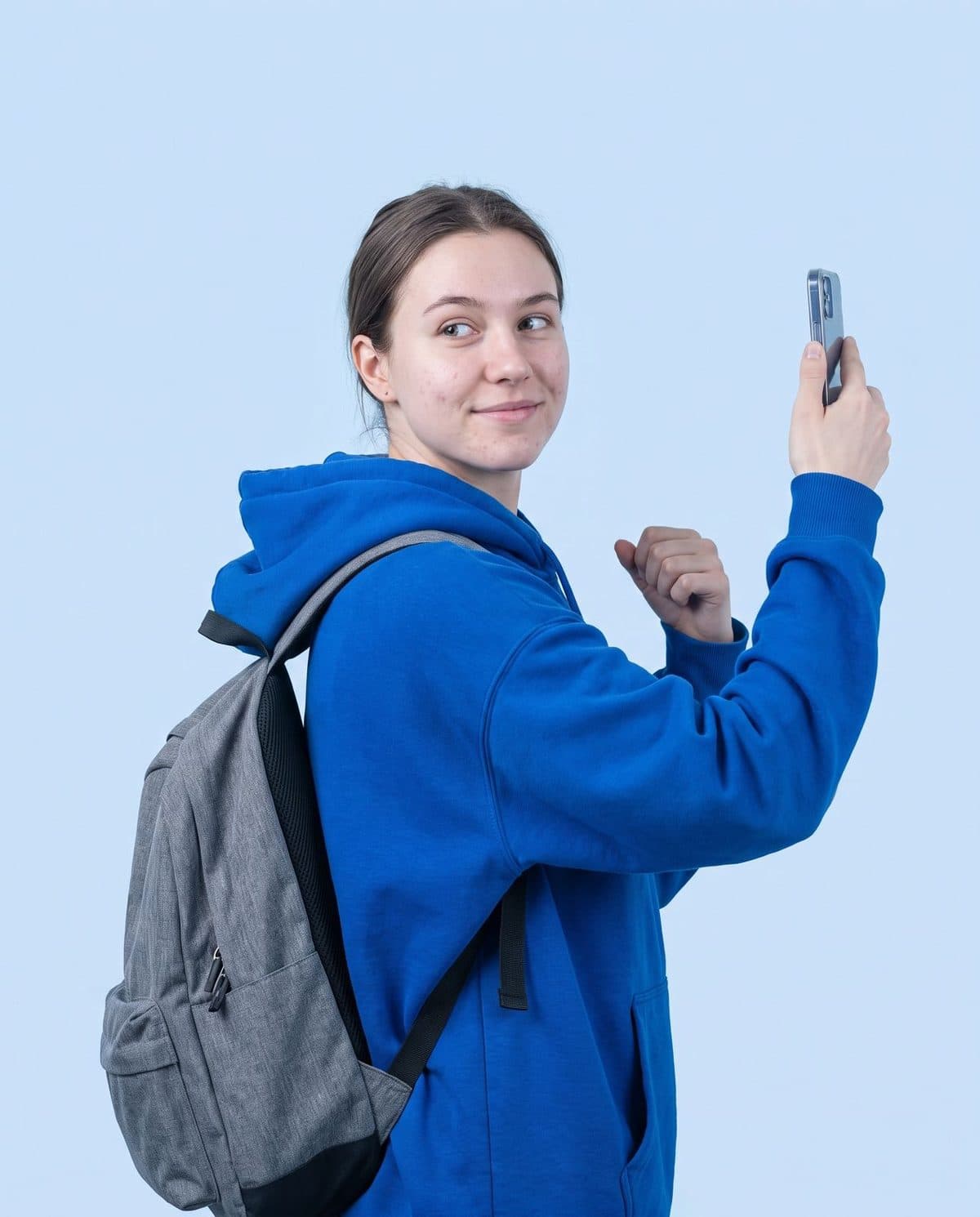 Young student in an electric-blue hoodie holding up a phone to record a lecture.